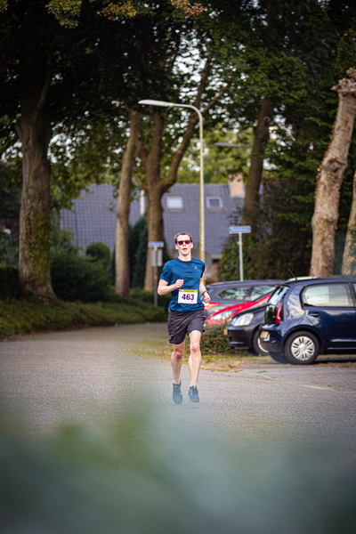 A man runs on a street, wearing a blue shirt and black shorts. He has the number 42 in white on his back.