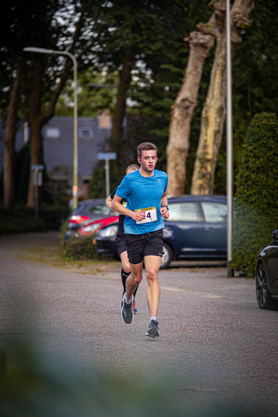 A runner in a blue shirt running past cars parked on the side of a road.