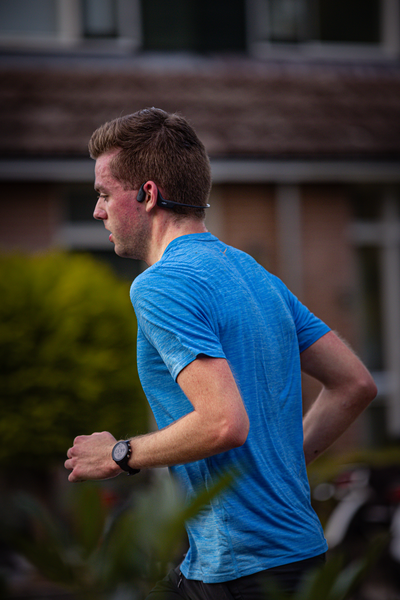 A young man wearing a blue shirt runs in front of a brick building.