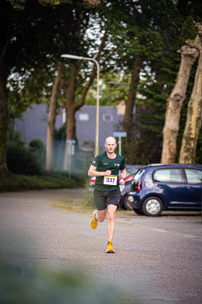 A runner is running on a street with a blue car parked near.