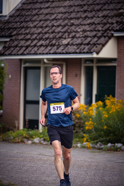 A man runs in the street while wearing a blue shirt and shorts. He has an 871 number on his shirt.