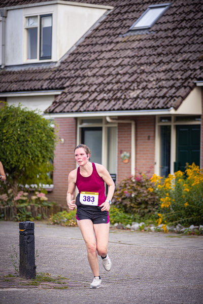 A woman running on a road, wearing number 38. She is in front of a building with a porch.