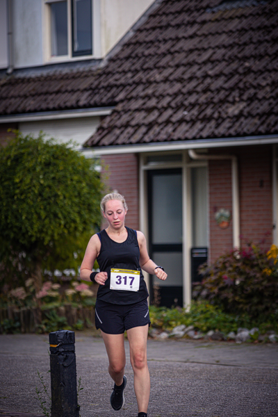 A blonde woman running down a street with the number 317 on her tank top.