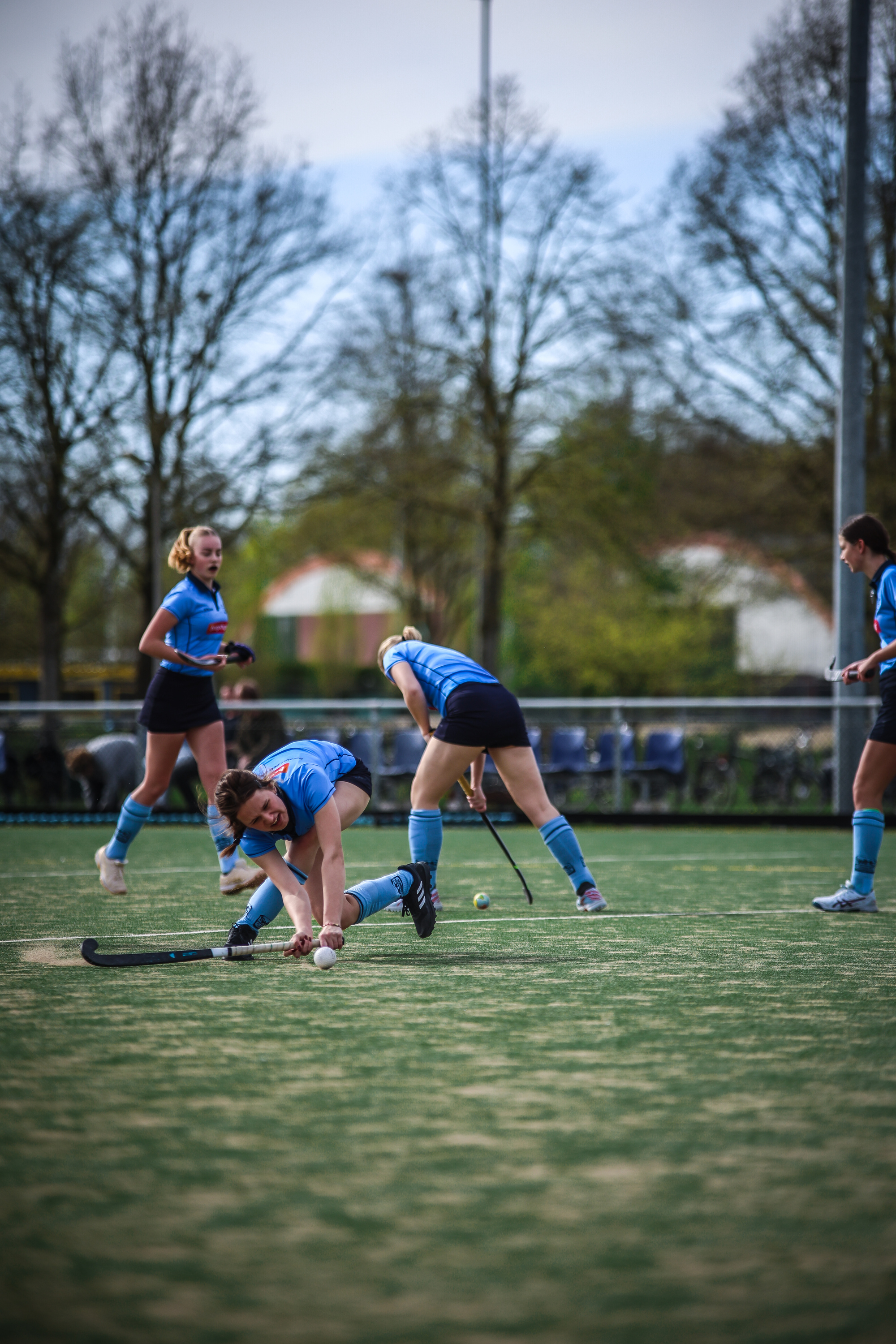 Three women playing hockey, one of them is on the ground.