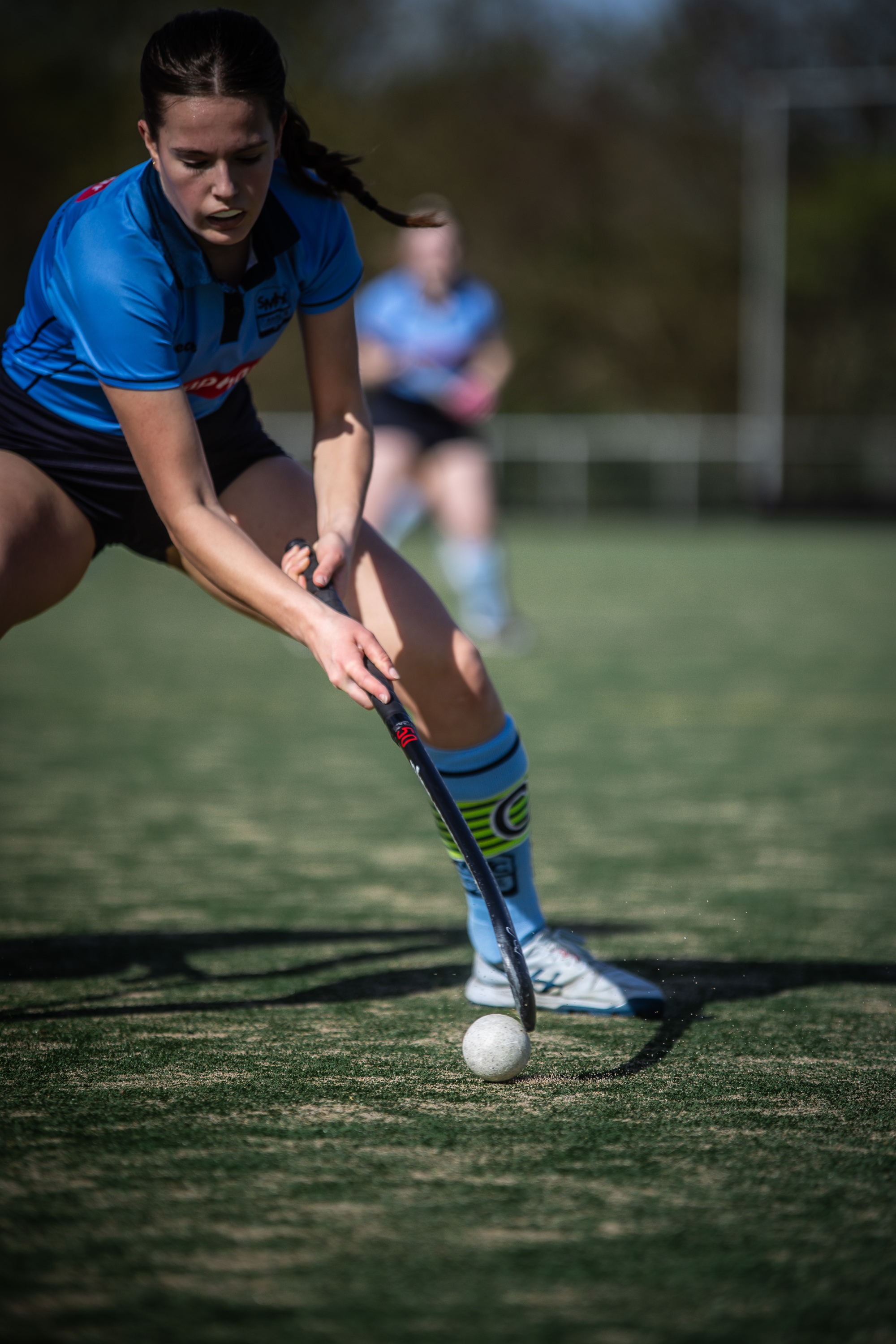 Two women playing hockey on a field with one woman having the ball.