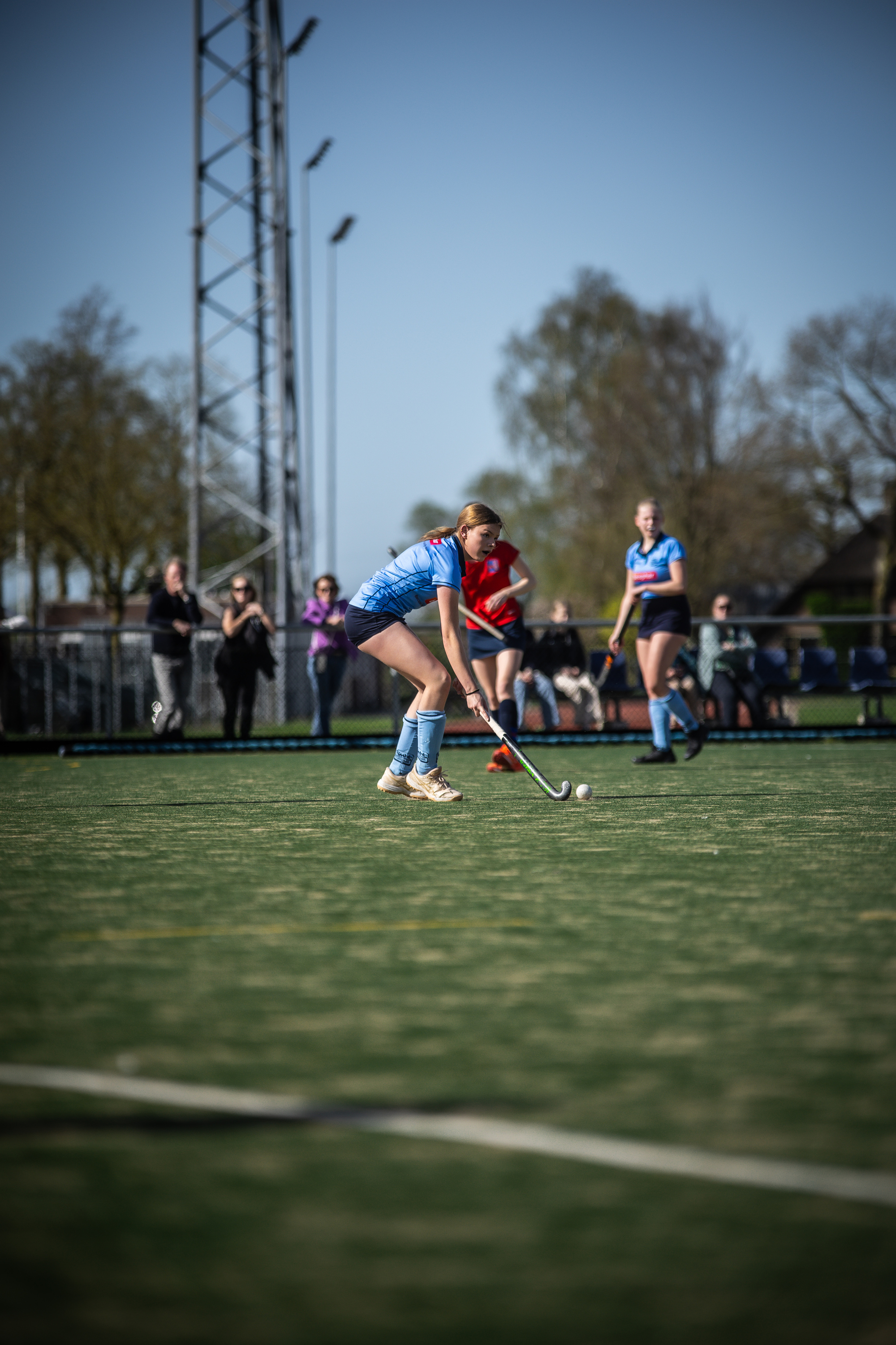 A woman in a blue jersey playing hockey in a field with several other people.