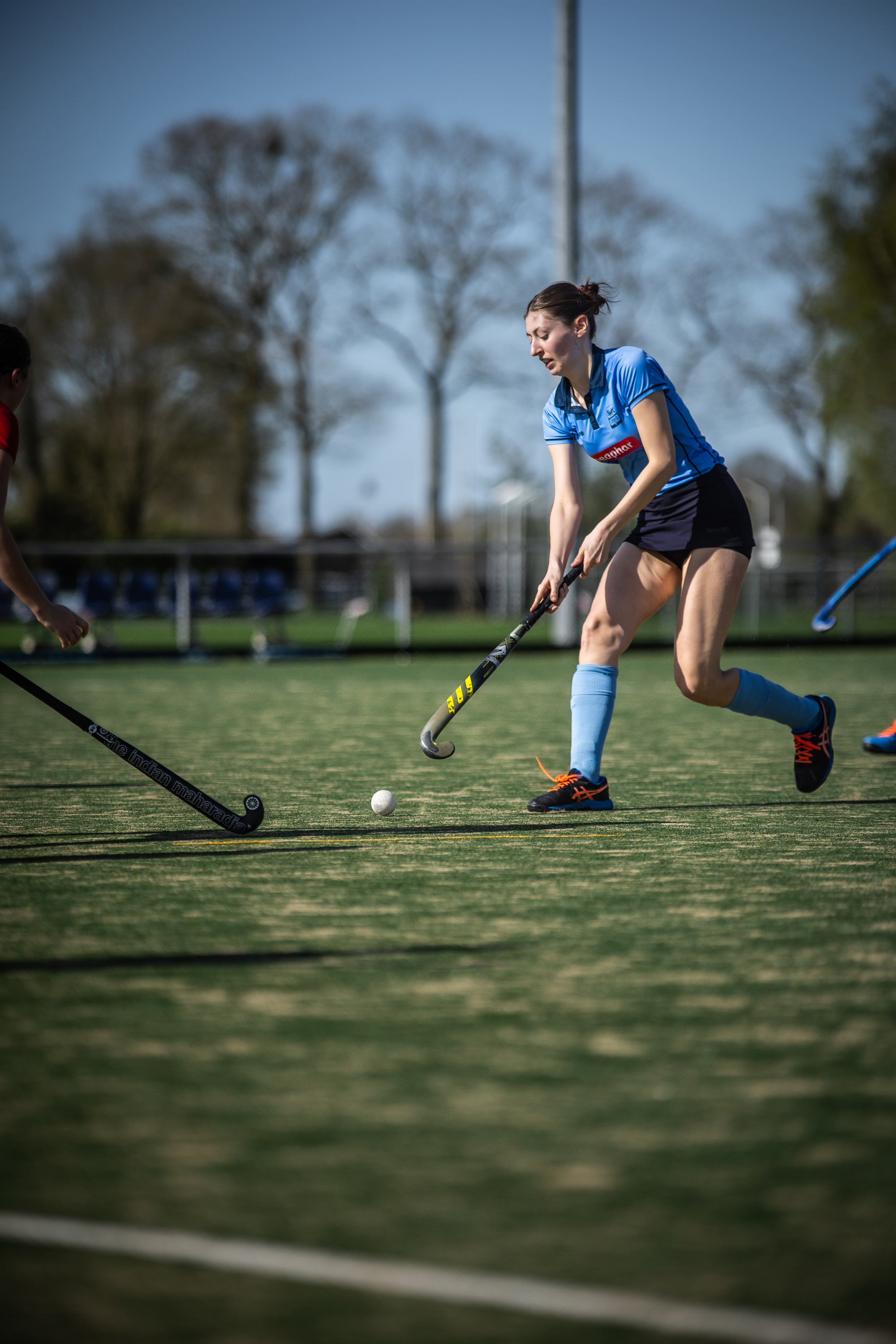 A young woman in a blue hockey uniform on an outdoor field with her hands outstretched.