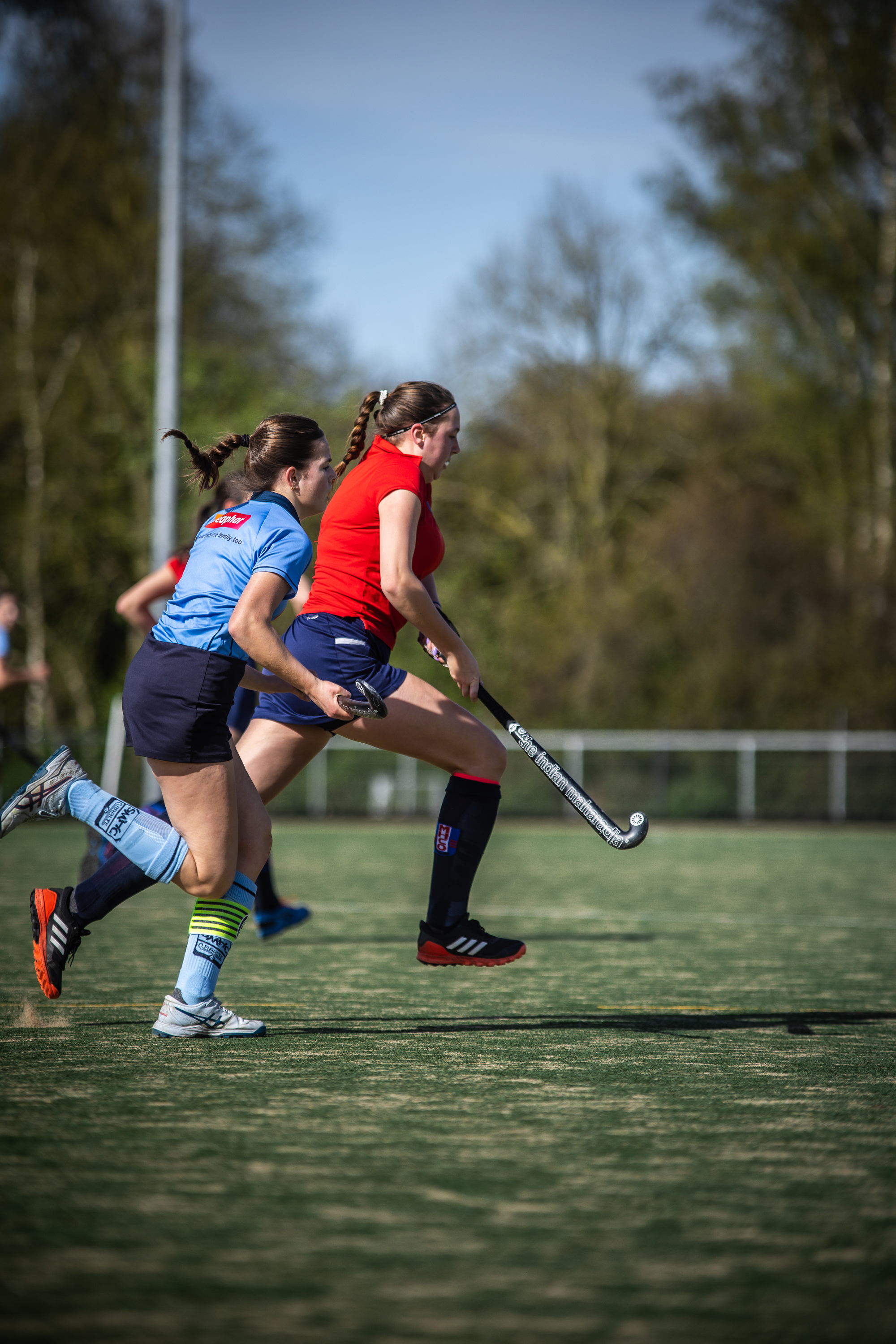 Two women playing a game of hockey, with blue and red jerseys on.