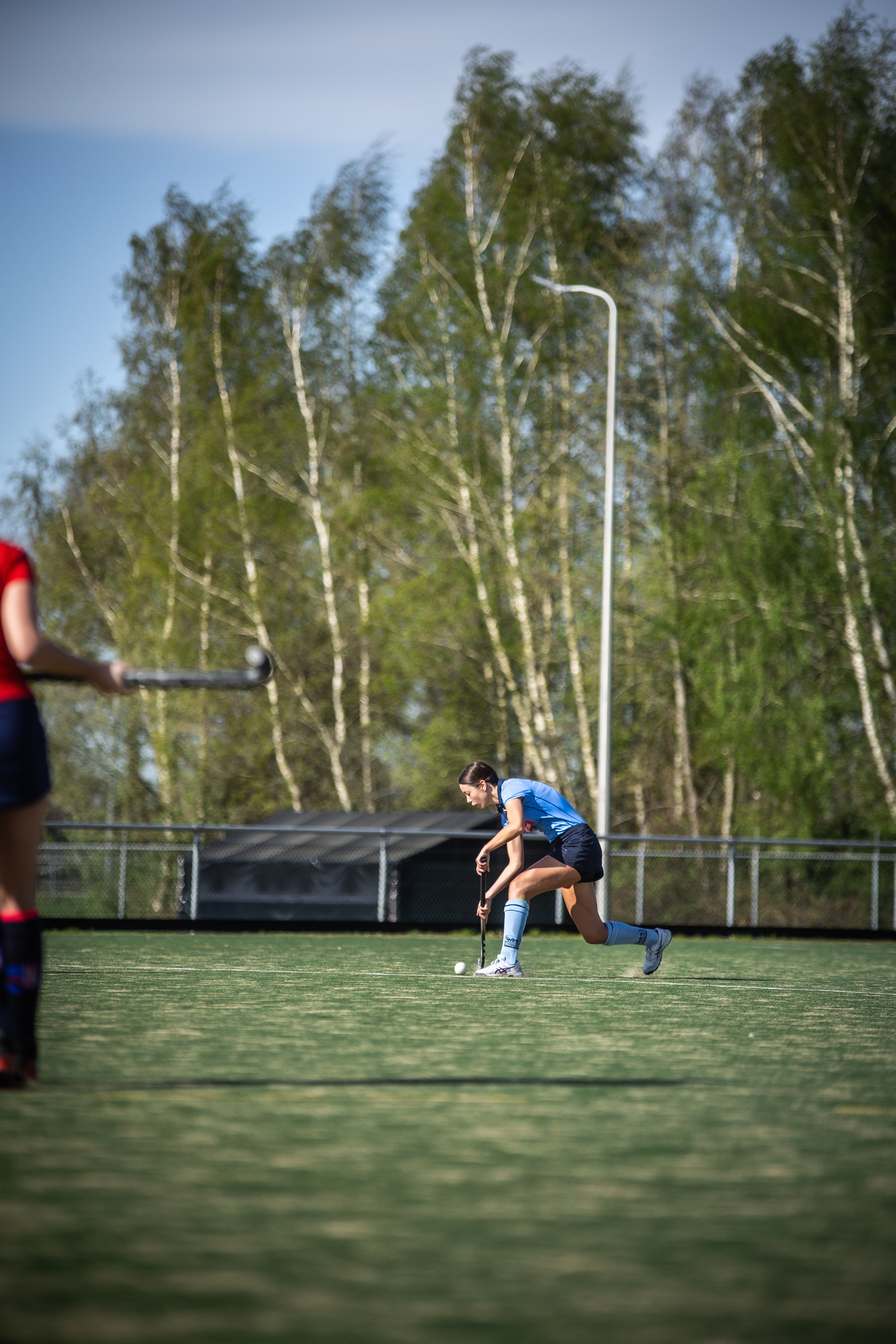 A woman in a blue jersey and shorts kicks a soccer ball on a field.