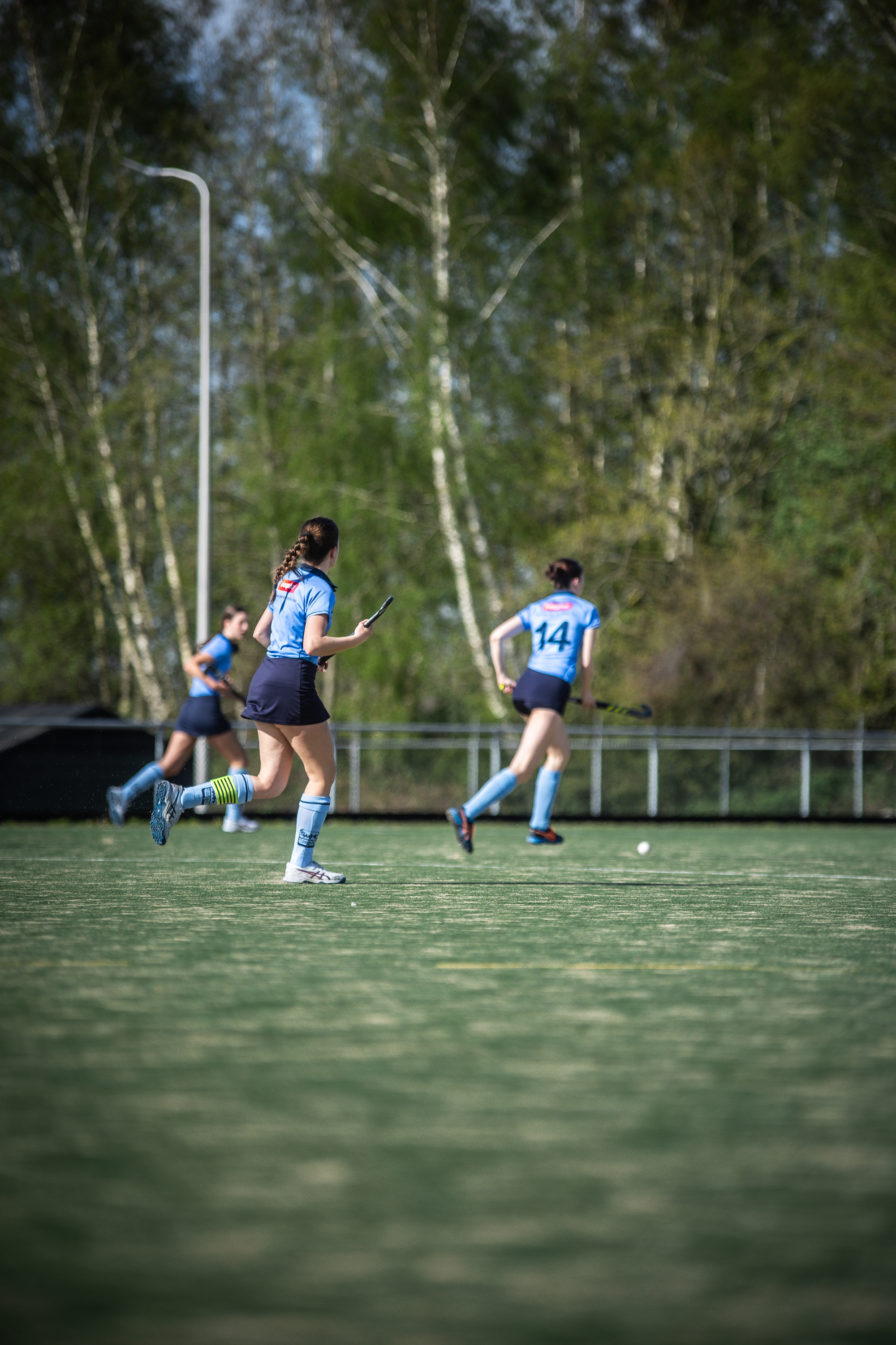 A group of people playing hockey in a field, all wearing blue uniforms with white numbers.