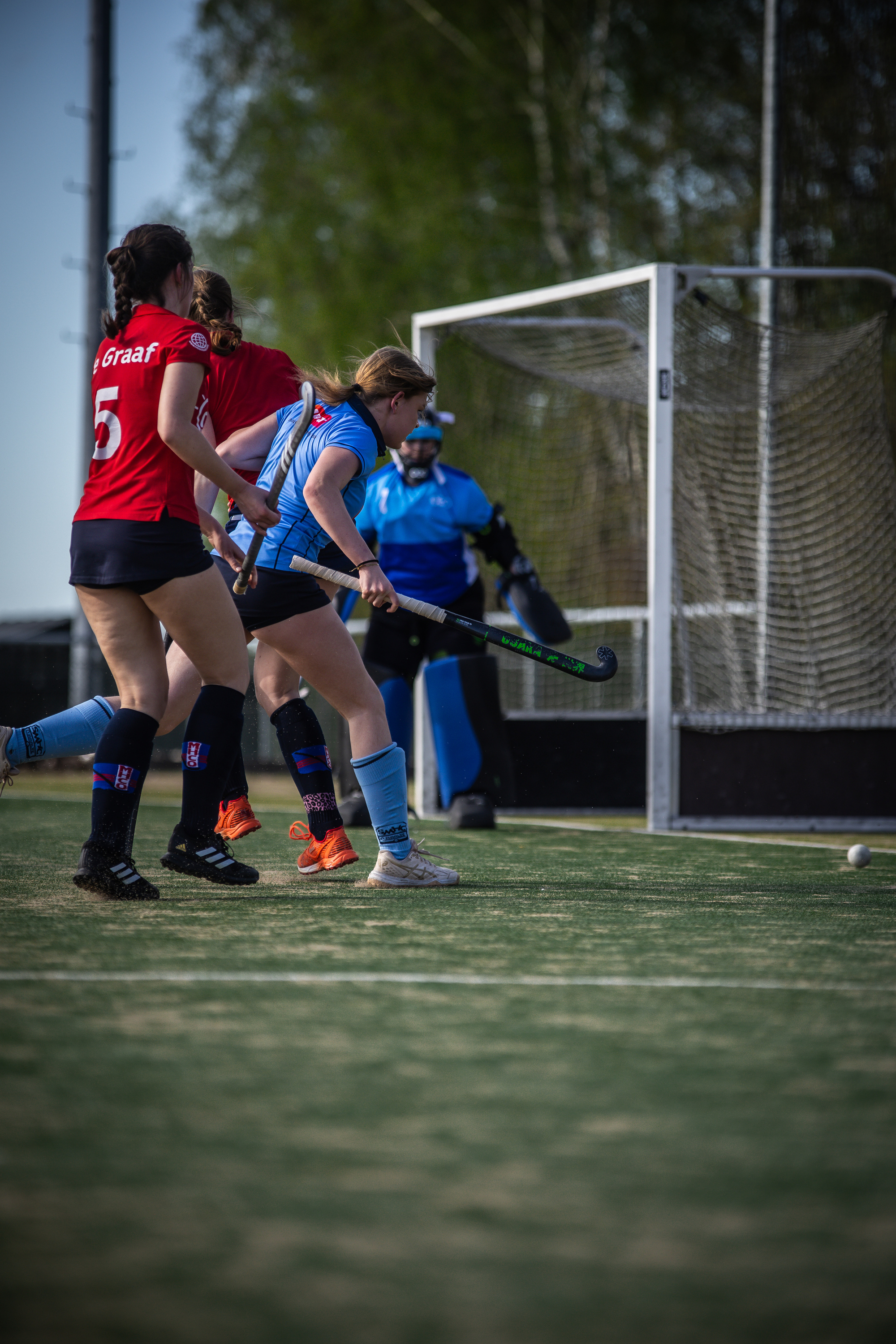 Two female hockey players are on a field with the number 5 and a referee.