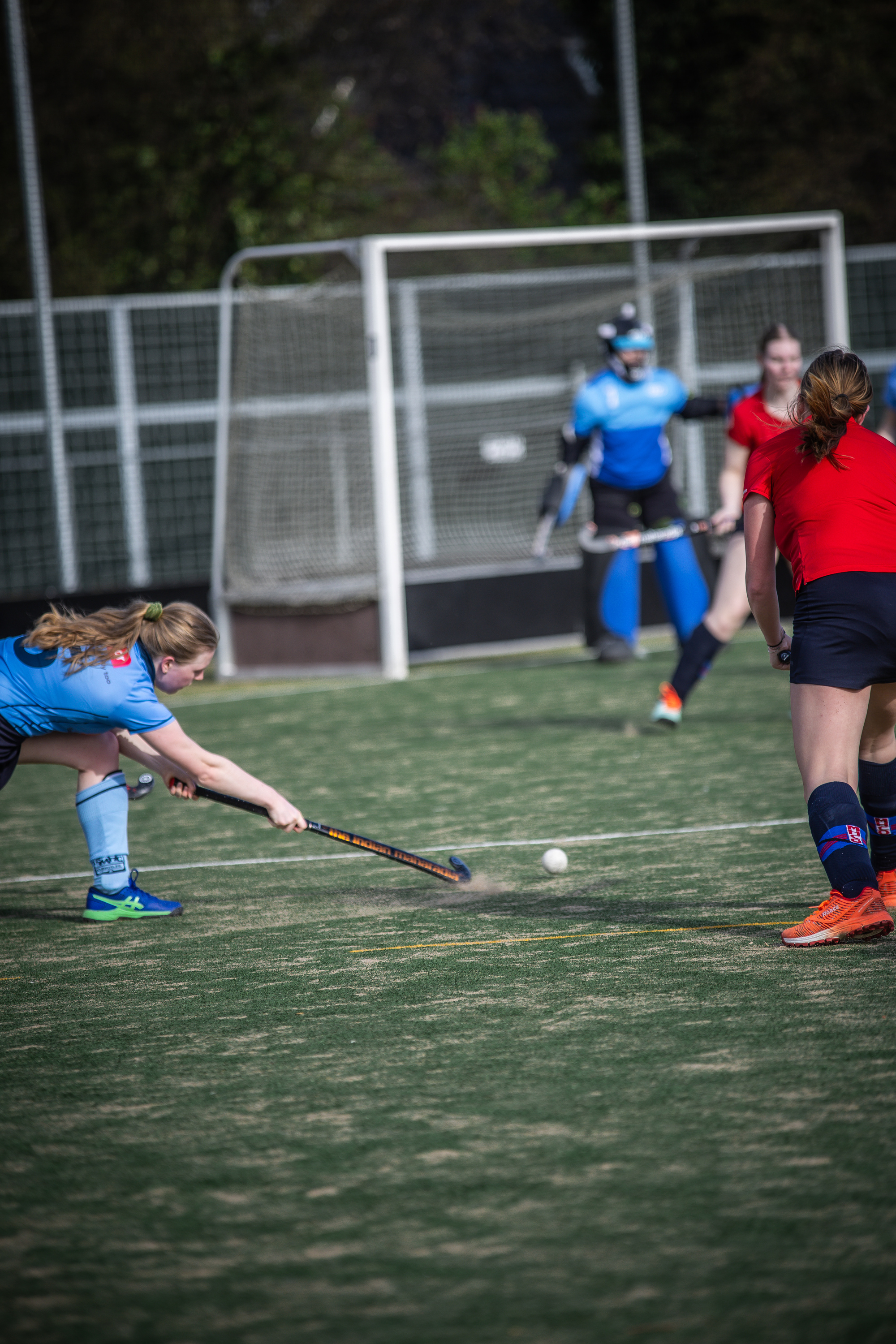 Three women playing hockey. One of them is about to hit the ball with her stick.