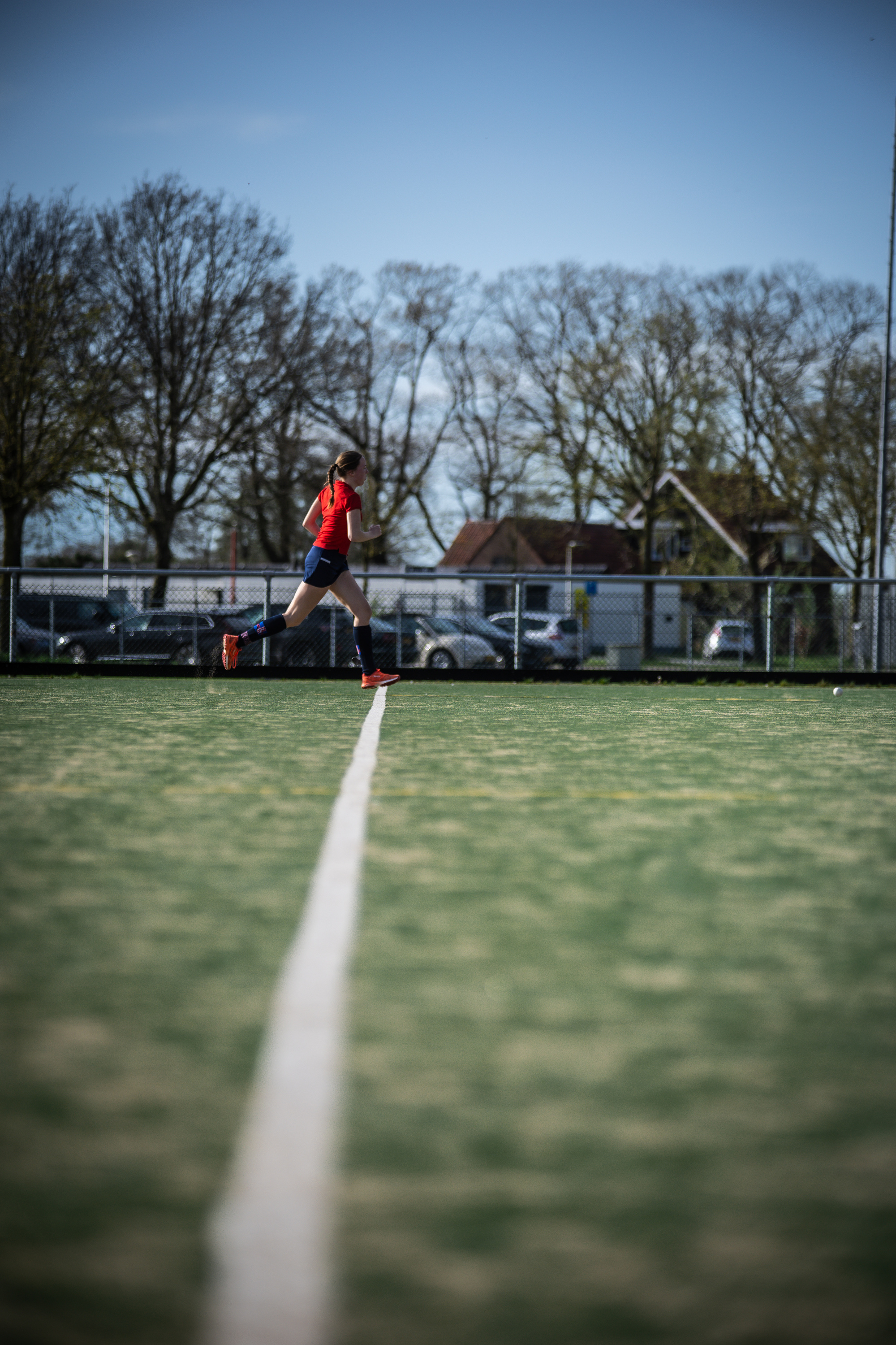 A man in a red shirt is playing hockey on a field near a park.