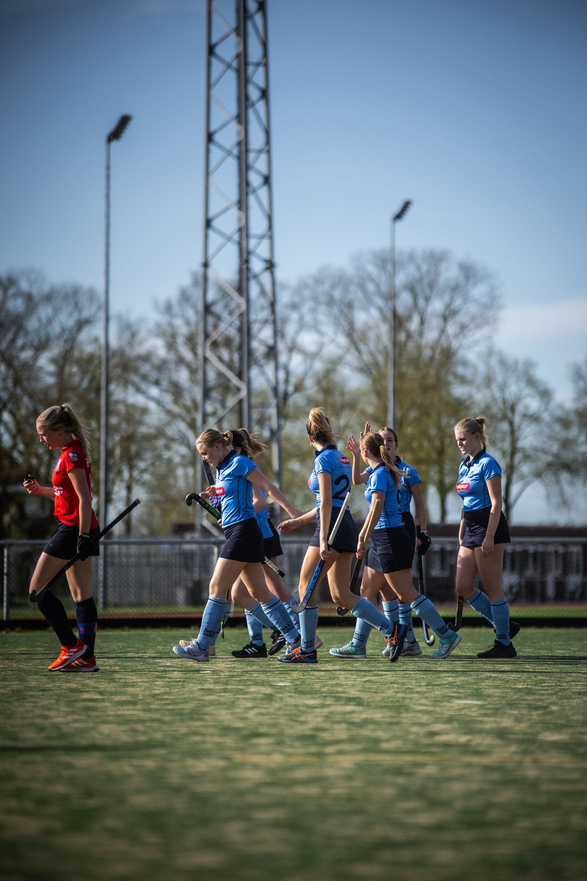 A group of 7 young female hockey players wear blue uniforms, sponsored by SMHC, and are seen on a field.