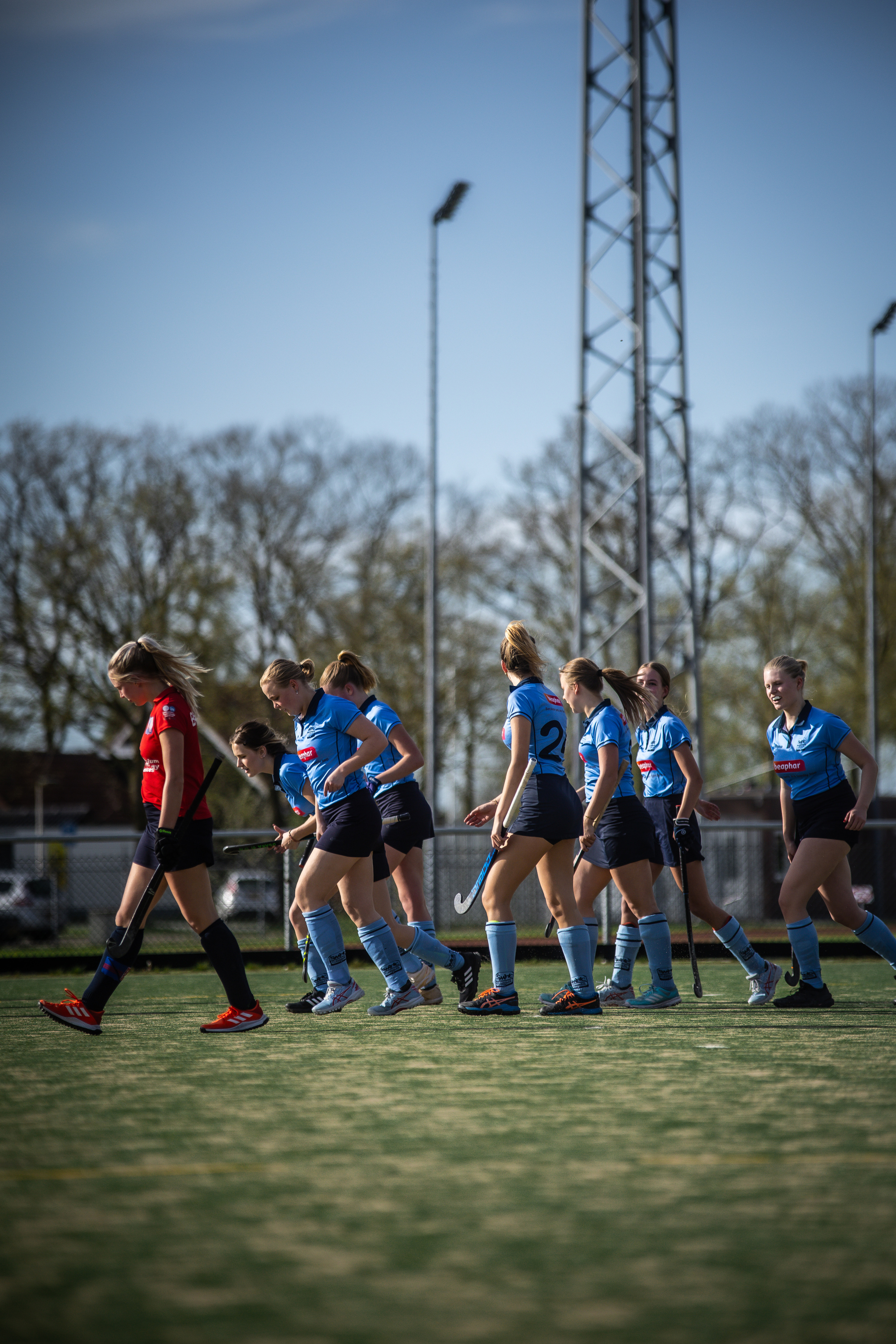 A group of women are standing on a green field holding hockey sticks, they are dressed in blue and white uniforms.