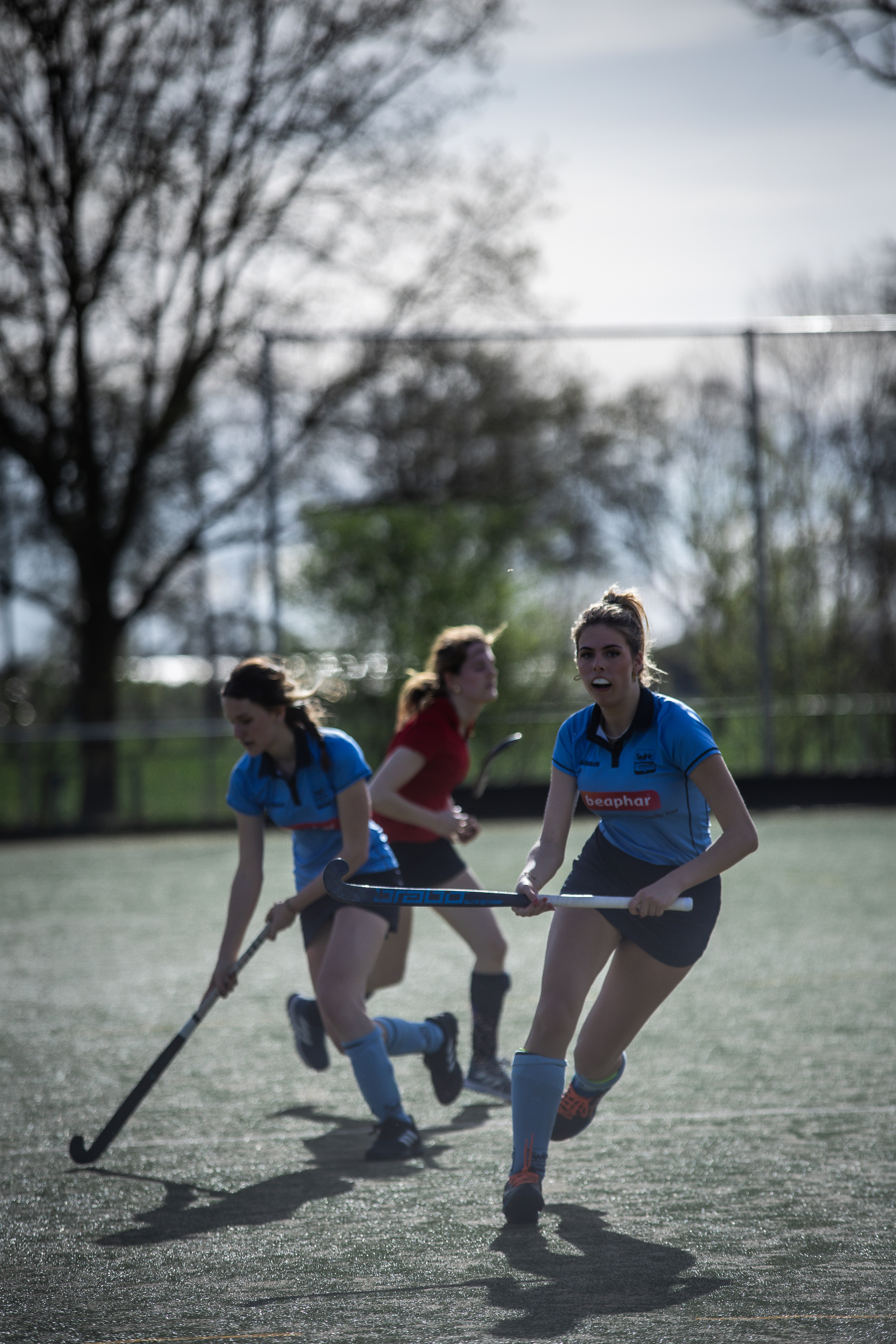 A group of women in blue hockey uniforms run with their sticks.