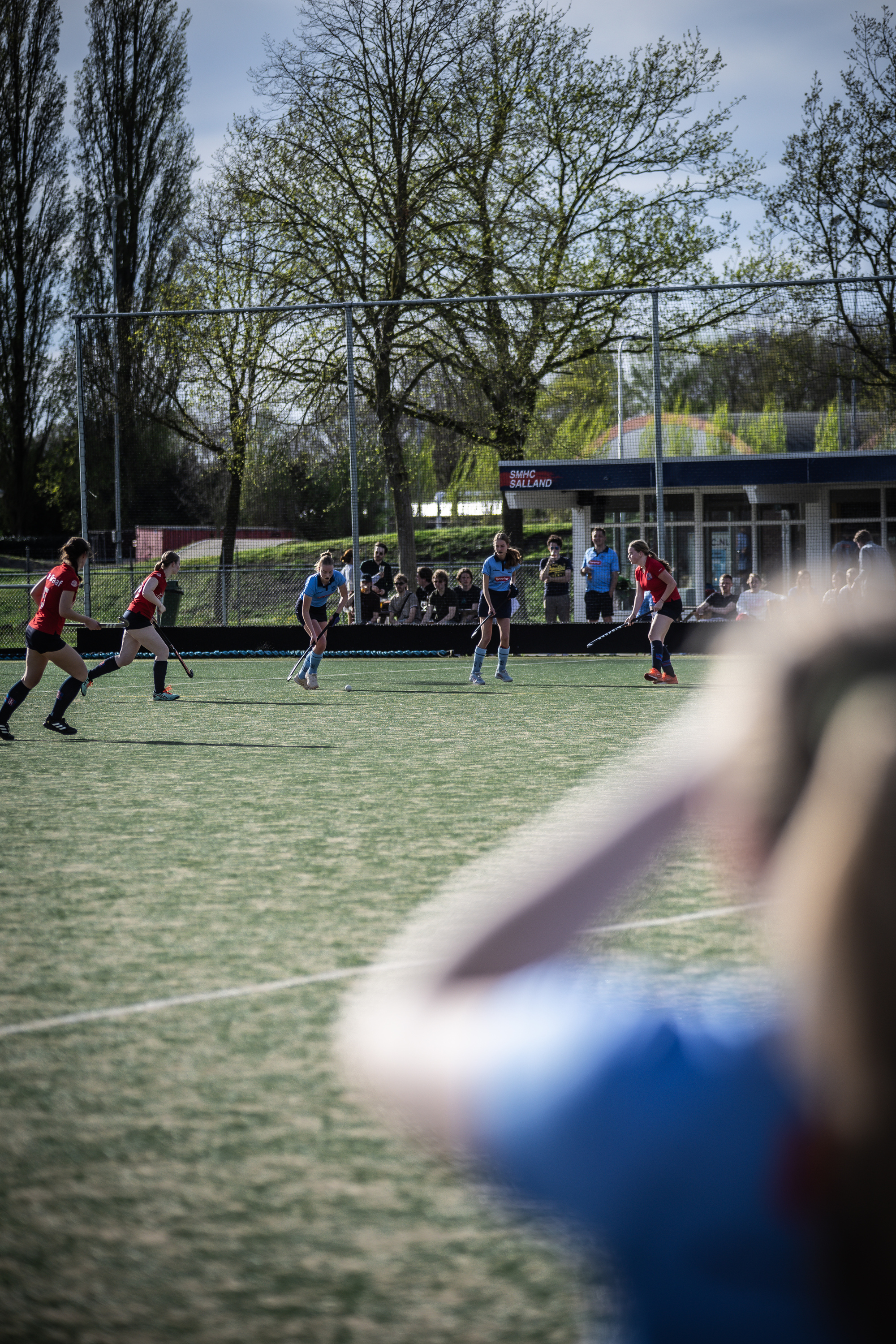 A photo of a hockey game between two teams. The goal is on the left side and there are spectators watching.