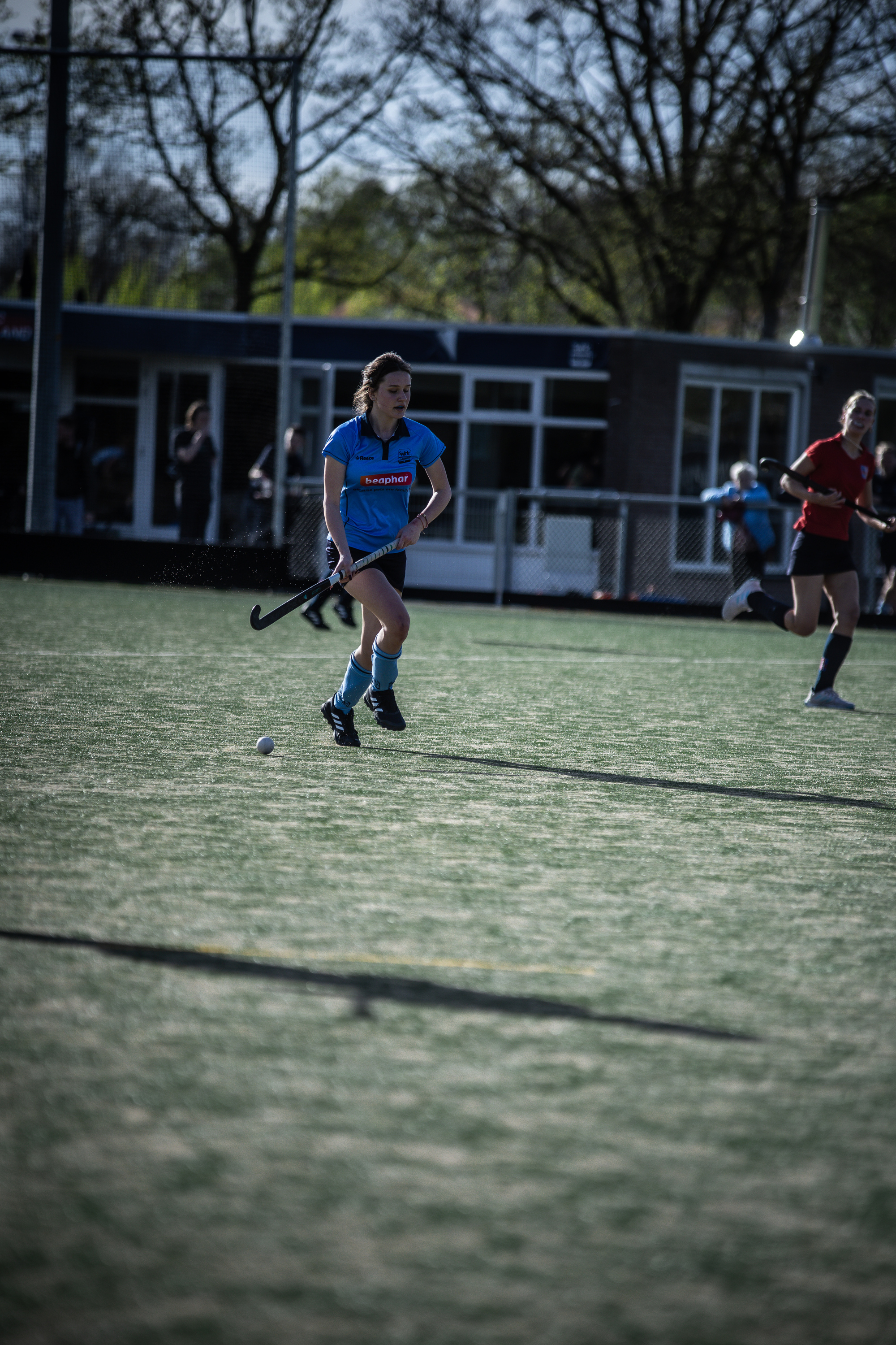 A woman in a blue jersey is about to hit the puck. The background features a building with the number 7 on it.