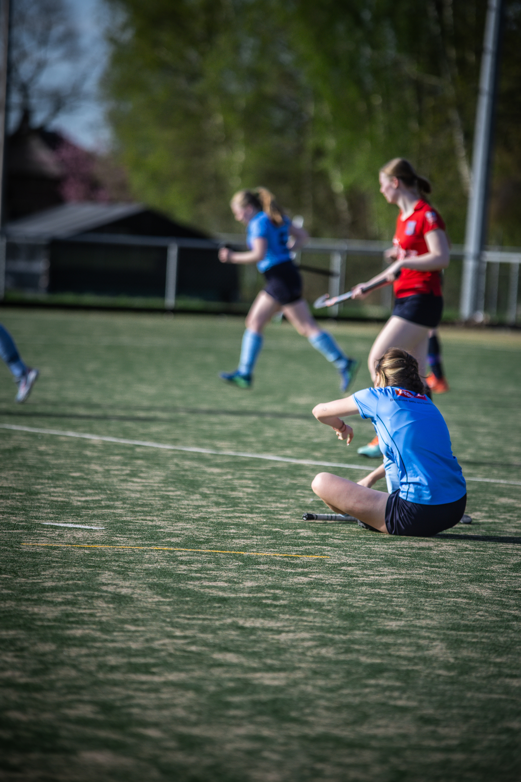 A group of female hockey players on a field with one player sitting on the ground.