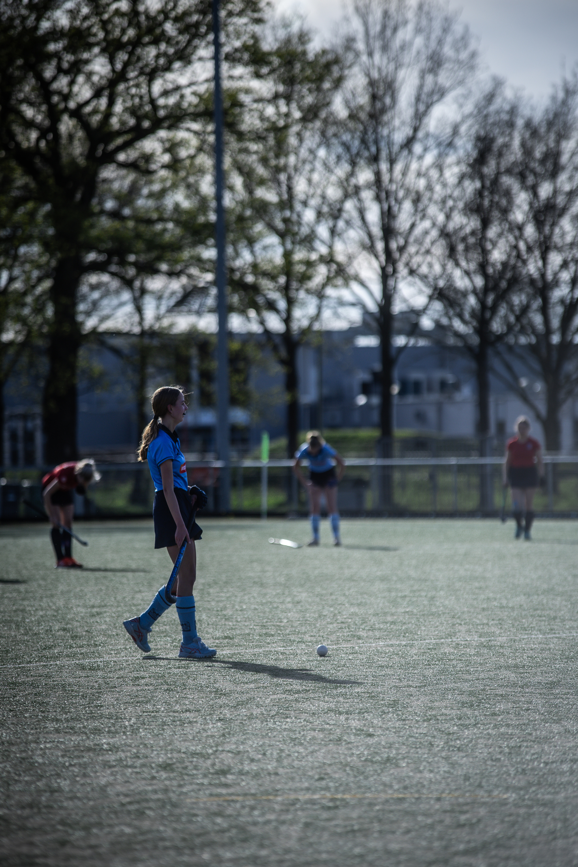 A girl is playing hockey on a field, and she's wearing a blue jersey with the number 12.