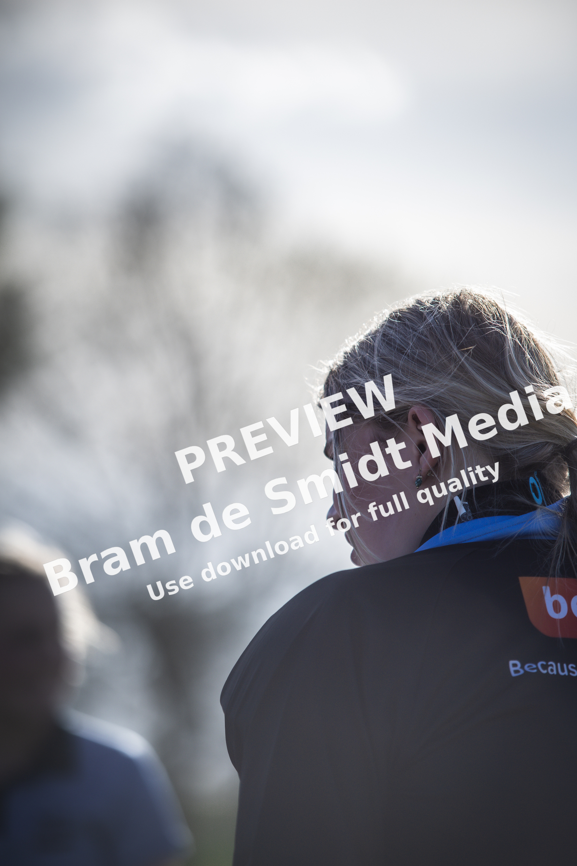 A woman wearing a black jacket with the letters BC on it is looking off to the side.