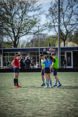 A group of athletes on a hockey field, one in a red jersey and two wearing blue.