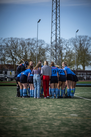 A young team of hockey players wear blue uniforms with the number 9 on the front, standing together for a photo on a field.