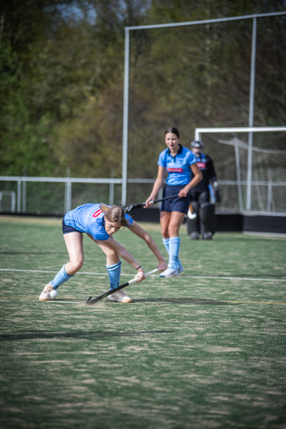 A girl wearing a blue hockey uniform on a field with another girl watching her.