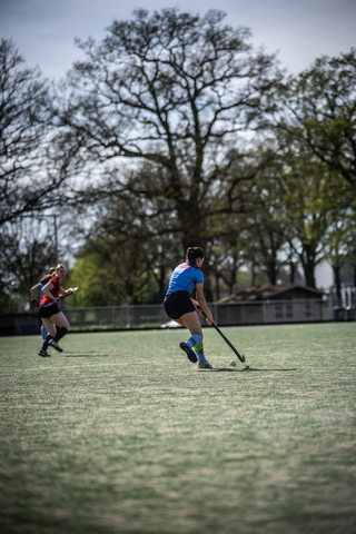 A woman wearing a blue shirt and black shorts plays hockey on a grassy field.