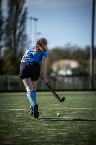 A hockey player, wearing a blue jersey with the number 21 on it, is in action. She holds her stick out to hit the ball.