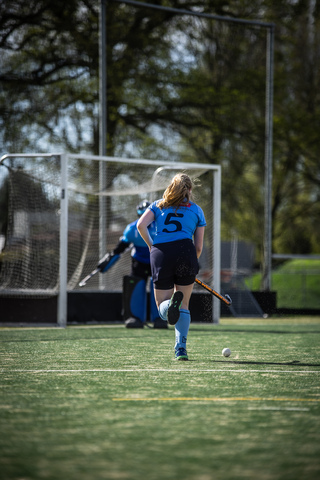 A hockey player in a number 5 jersey jogs across the field with her stick, near the goal.