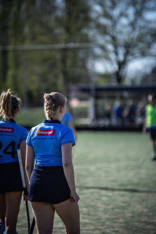 A woman is playing field hockey on a field. She is dressed in a blue uniform with the number 24 on it.