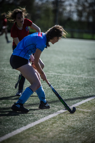 A young athlete in a blue and black jersey is preparing to hit the puck with her hockey stick.