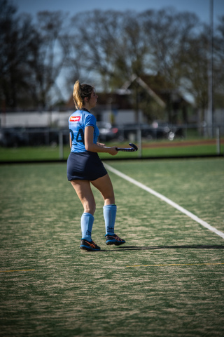 A female sports player in a blue uniform with the number 10 on her back. She is standing on a field holding a hockey stick.