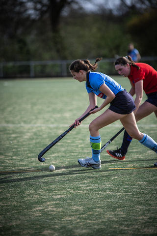 Two women in hockey gear play a game of field hockey.