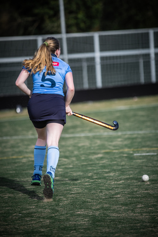 A girl playing hockey on a field, she's wearing blue and has the number 5 on her jersey.