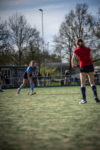 Two women wearing sports uniforms play a game of hockey on a court in April.