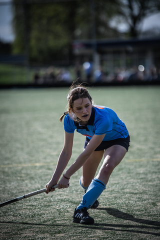 A woman in a blue jersey and shorts playing hockey on the field.