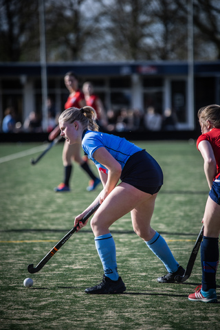 Two young girls playing hockey, wearing blue uniforms with red accents.