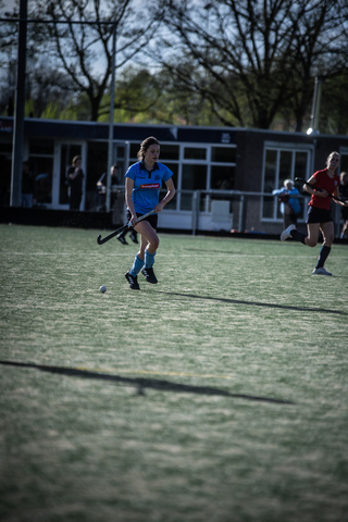 A woman in a blue jersey is about to hit the puck. The background features a building with the number 7 on it.