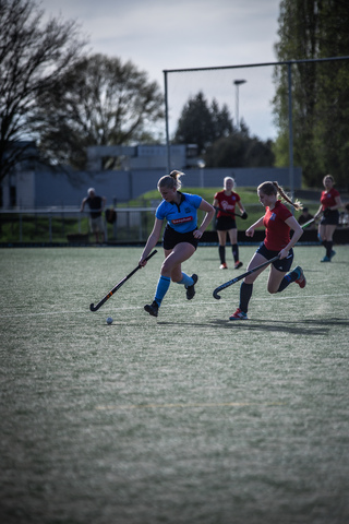 Four young women play a game of hockey on the field.