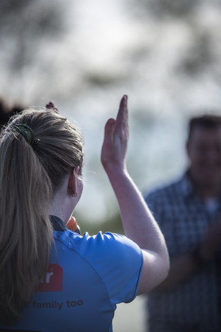 A woman in a blue shirt with the words family too on the back of it is giving a thumbs up.