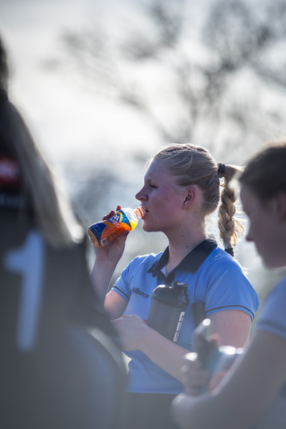 Two women are standing outside, one with a blue shirt holding a can of soda.