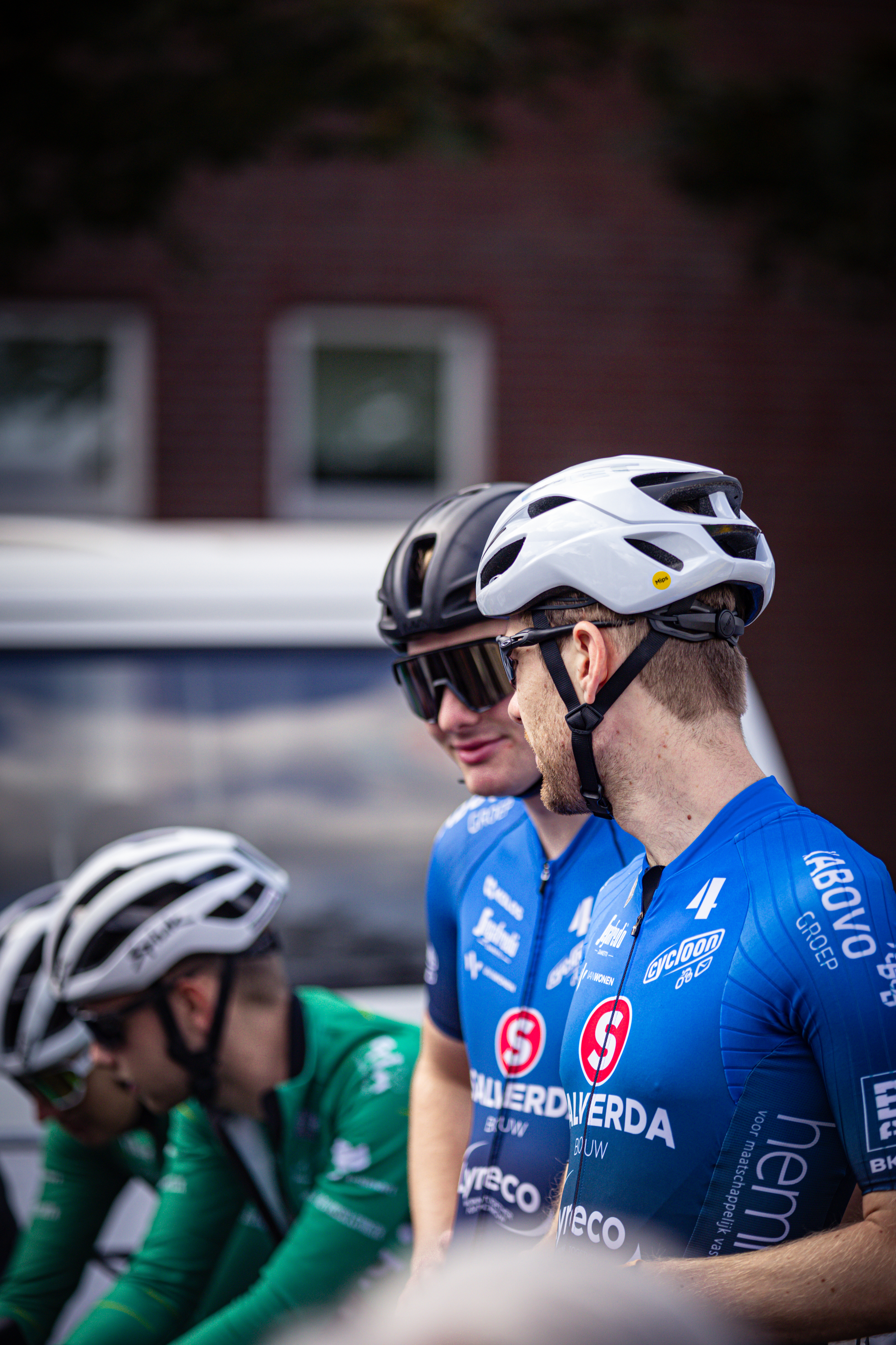 Two male cyclists in blue and white gear, one of them with a red number 1 on his shirt. They are standing next to each other.