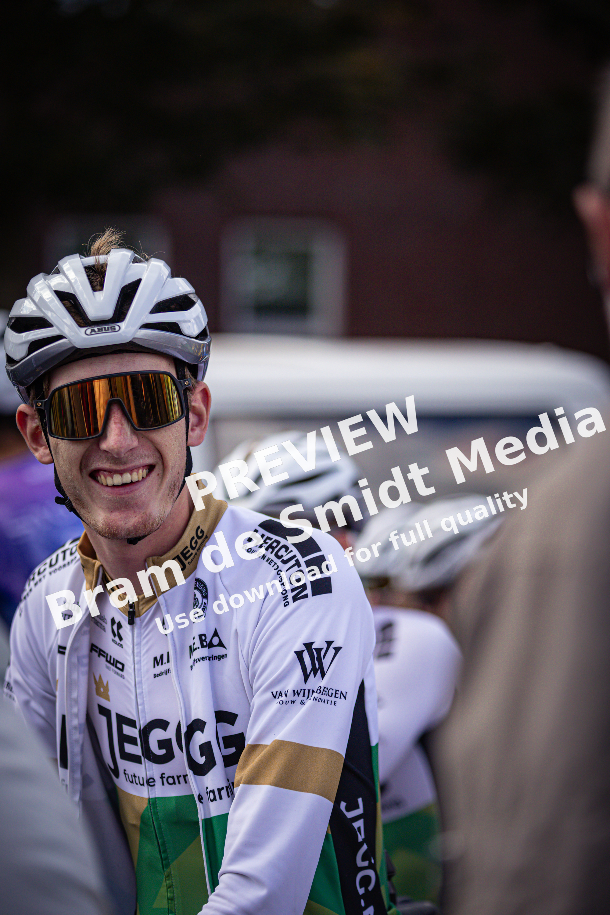 A cyclist wearing a white and yellow jersey with "TEEGE" on it. He's also wearing glasses.