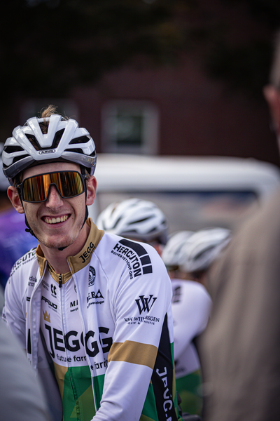 A cyclist wearing a white and yellow jersey with "TEEGE" on it. He's also wearing glasses.