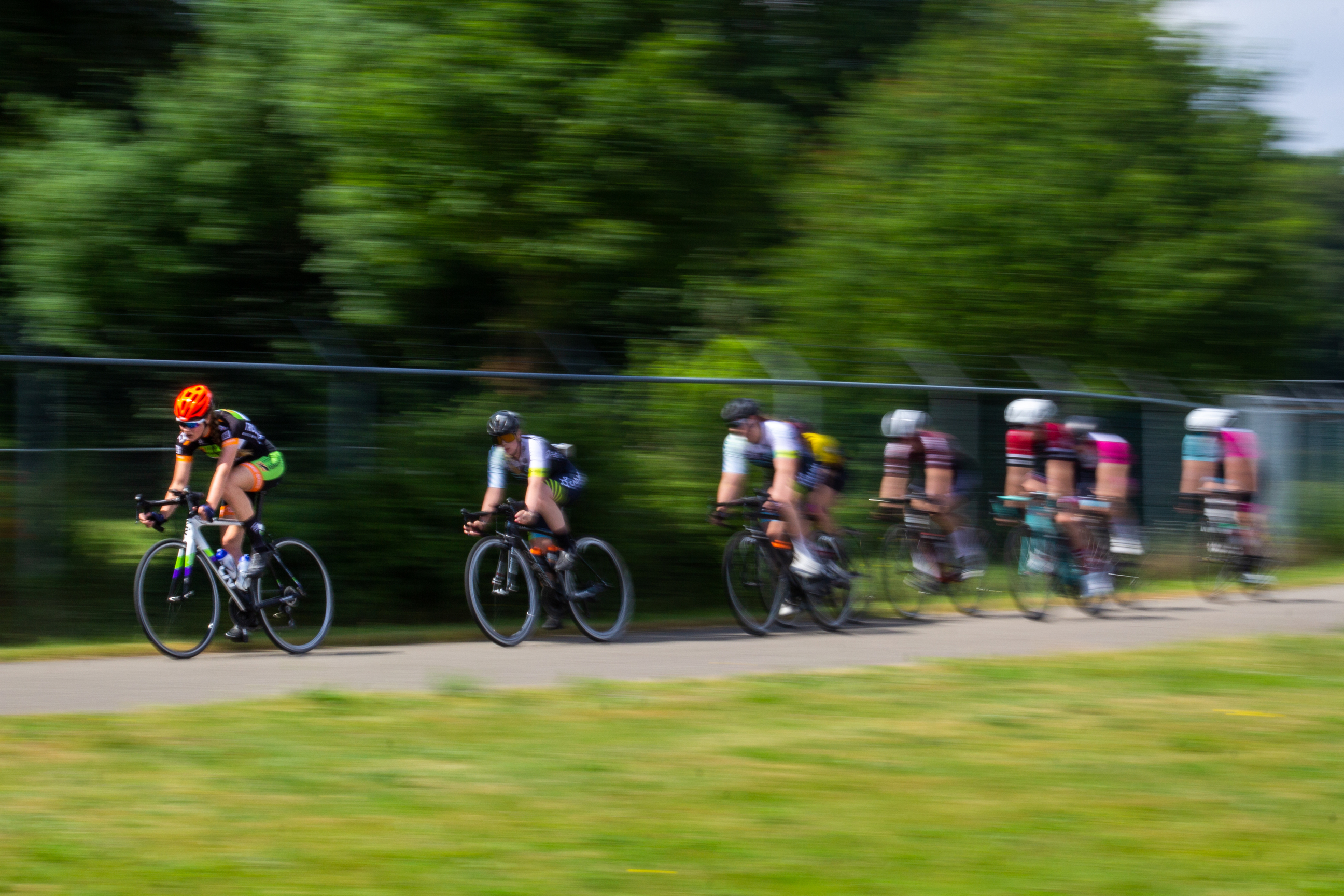 Several cyclists participating in a race, one of which is wearing an orange helmet.