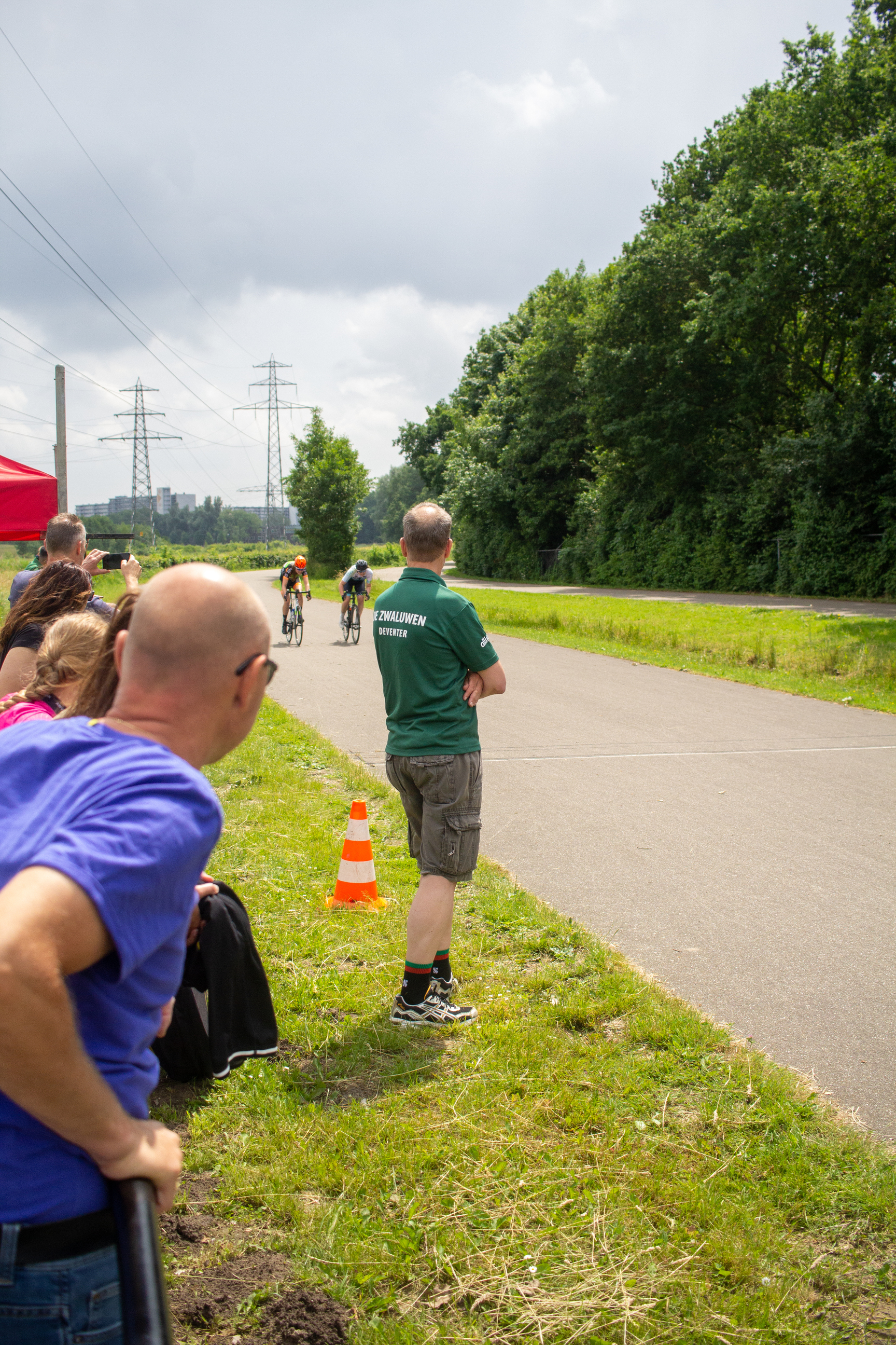 A man is standing at the edge of a road where cyclists are passing by.