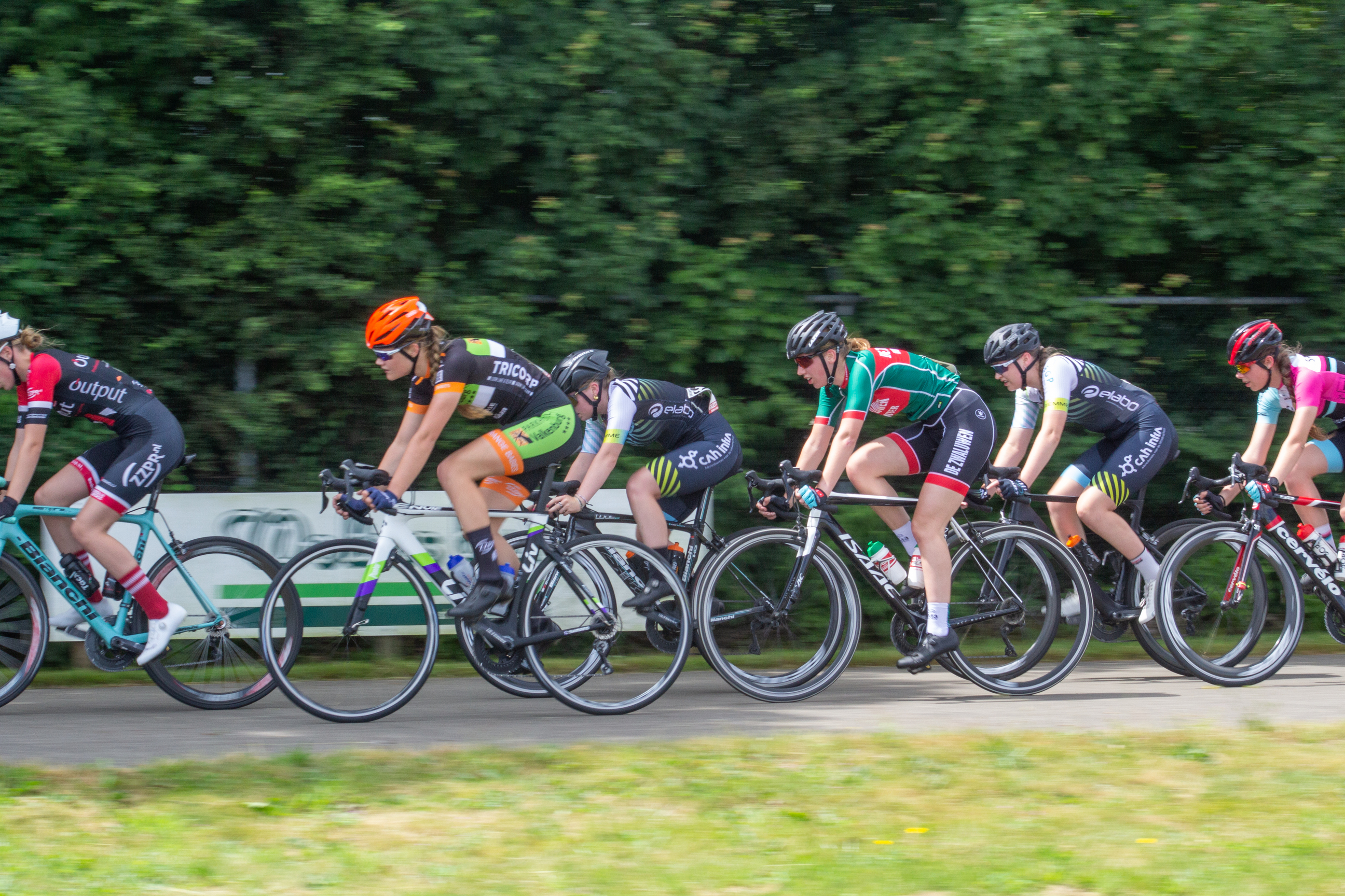 A group of cyclists riding on a road with numbers and letters on their jerseys.