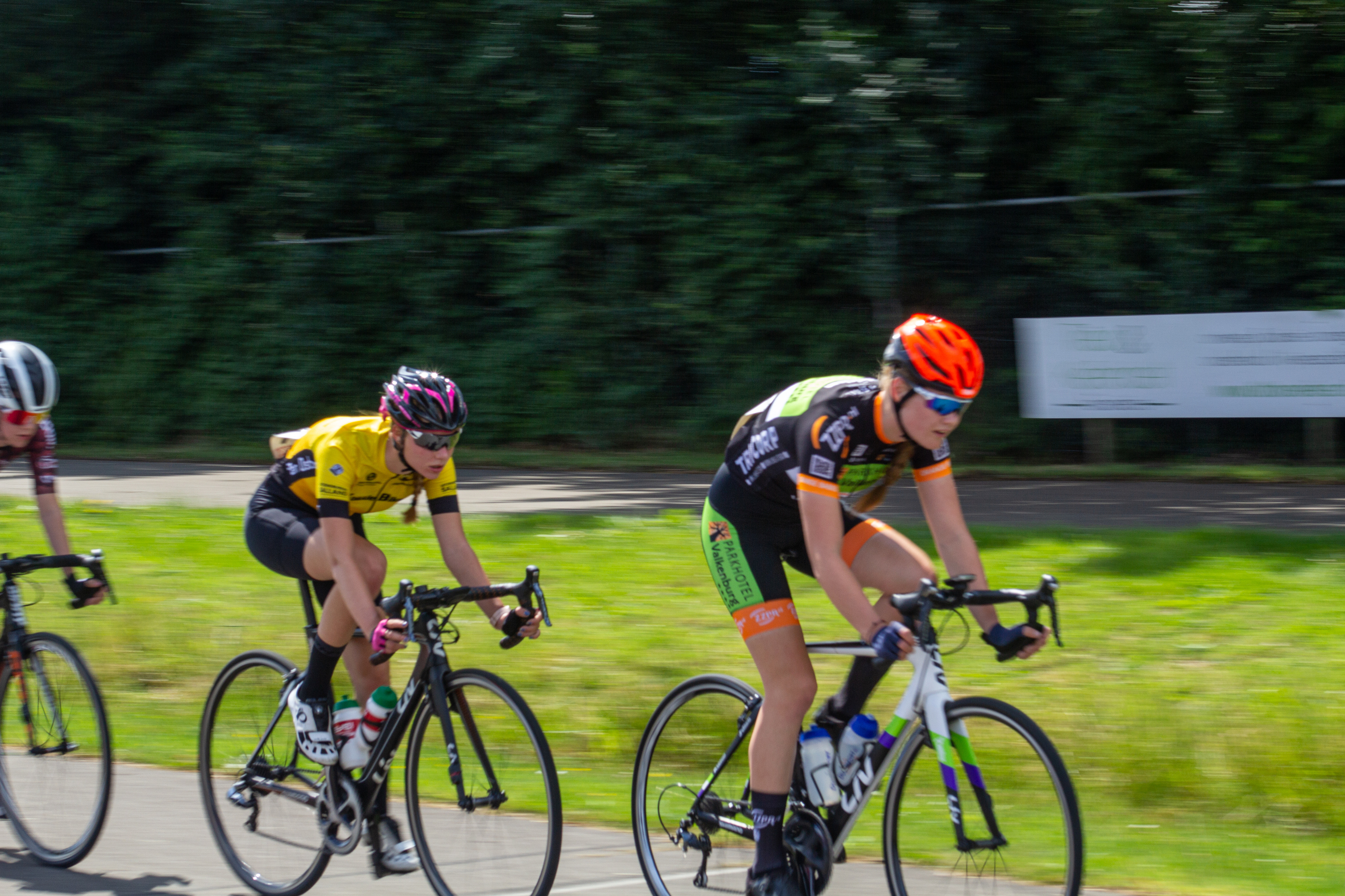 Two cyclists racing in a race and one is wearing an orange helmet.